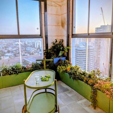 עגלת שירות מעוצבת למרפסת עגלת משקאות ירוקה מינימליסטית עם כוס מים ונענע, על רקע נוף עירוני ושקיעה.